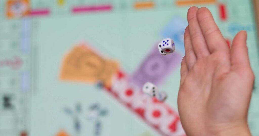 hand rolling dice over monopoly game board