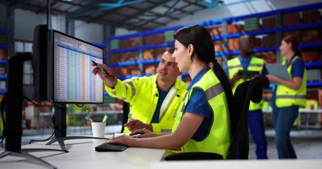warehouse manager and employees looking at numbers on computer monitor