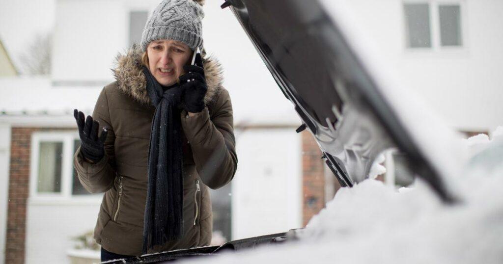 distraught woman talking on phone over snow covered car with hood up