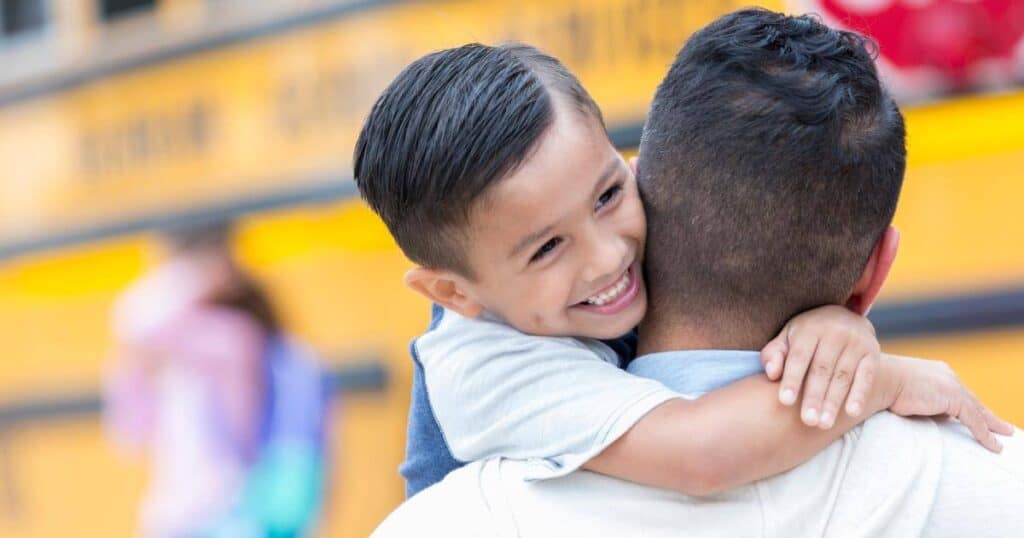 a son hugging his father after getting off the school bus