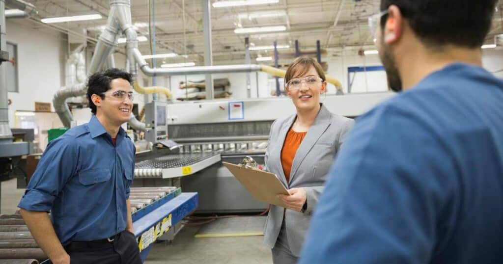 manufacturing leader on production floor taking notes while talking with employees