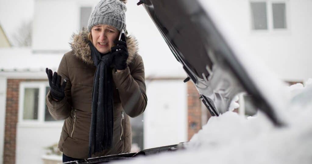 distraught woman talking on phone over snow covered car with hood up